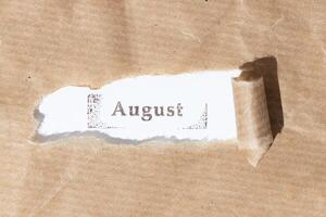 Brown paper torn stripe with ink stamp text August on white paper background photo