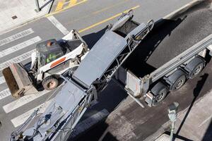 Road maintenance with a Milling machine working and removing asphalt from the city road and pouring it into a truck photo