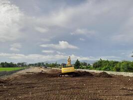 West Lombok Regency, Indonesia - February 4, 2024. Outdoors, a Backhoe is at work leveling the ground for a housing site, with a blue sky in the background. photo
