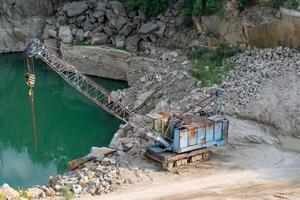 Mining in the granite quarry. Working mining machine - old crane. Mining industry. photo