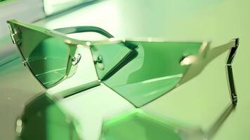 These smart sunglasses have a unique shape with the lenses extending beyond the edges of the frames. The lenses themselves are a vibrant green while the frames are a shiny silver wit video