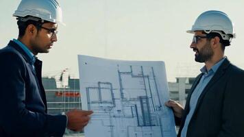 Architects and engineers discussing blueprints at a construction site, with the building framework visible in the background. The interaction and planning process are the focus. video