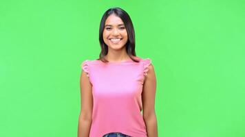 A woman in a pink shirt is smiling and posing for a photo. The green background adds a pop of color to the scene video