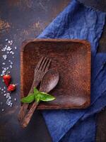 Empty wooden plate, cutlery, salt, pepper and basil photo