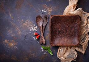 Empty wooden plate, cutlery, salt, pepper and basil photo