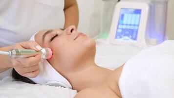 Close-up portrait of a beautiful woman with closed eyes and apparatus for skin rejuvenation. Beauty salon procedures. RF lifting. Microcurrents. video