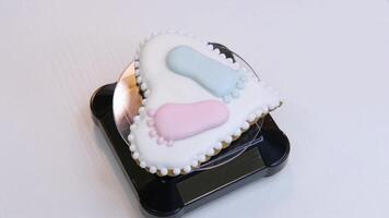 A heart-shaped gingerbread with a baby heels depicted on it spins on a plastic tray. An example of a gift for the birth of a child. video