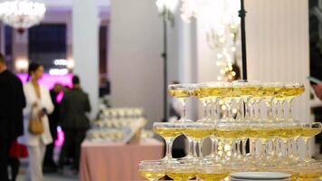 A pyramid of champagne glasses at a party against the backdrop of a hall with guests. champagne pyramid video