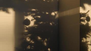 The shadow of the Christmas tree on the sand-colored wall. The Christmas ball sways from side to side. Abstract video