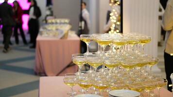 A pyramid of champagne glasses at a party against the backdrop of a hall with guests. champagne pyramid video