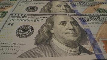 A close-up shot of a stack of one hundred dollar bills, showing the portrait of Benjamin Franklin and the details of the currency. Moving camera video