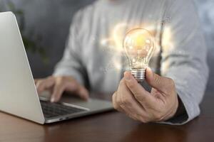 A classy businessman holding a colorful light bulb with shining circles in front of dark background concept. photo