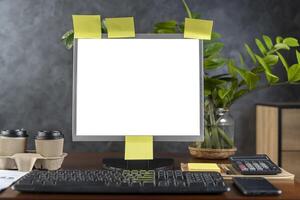 Computer monitor with white blank screen on the business desk with calculator, keyboard at home office over dark wall backgroun. photo
