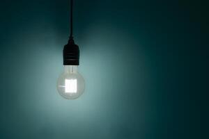 Illuminated light bulb hanging against a teal backdrop, casting a soft glow photo