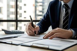 Man in suit writing at desk with window, documents and calculator photo
