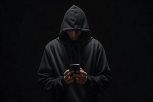 Hacker in black hoodie using smartphone in in the dark, cybercrime concept photo