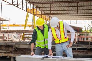ingeniero y capataz trabajador equipo con planos comprobación proyecto a el prefabricado hormigón fábrica sitio, ingeniero y constructores en sombreros duros que se discute en construcción sitio foto