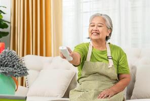 Smiling Asian senior woman with air conditioner remote control in living room, Woman switching on air conditioning photo