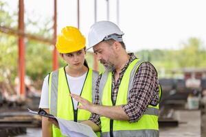 ingeniero y capataz trabajador equipo con planos comprobación proyecto a el prefabricado hormigón fábrica sitio, ingeniero y constructores en sombreros duros que se discute en construcción sitio foto