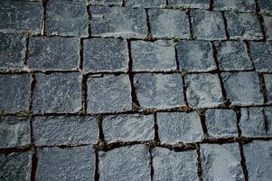 The texture of dark paving stones. Top view of the cobblestone pavement. An old stone sidewalk. The texture of the paving stones. The background is made of cobblestones, the road is made of cobbleston photo