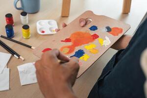 Artist Mixing Paint on Palette with Brushes and Paints on Wooden Table in Studio photo