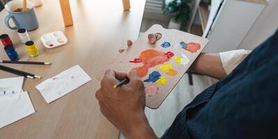 Artist Mixing Paint on Palette in Studio with Brushes and Supplies on Wooden Desk photo