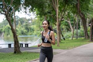 Young Woman Jogging in Park with Water Bottle, Enjoying Outdoors Exercise in Green Natural Environment photo