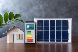 Energy efficiency mobile app on screen rating with arrows and house, text. Smart home display and model house with solar panel. photo