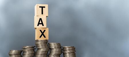 Tax concept with wooden blocks on stacked coins. Word TAX written on wooden cubes on stacked coins on dark background. Panoramic images have free space. photo