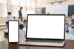 Front view, blank screen of black digital laptop and smartphone with tablet on the wood table. Education software website technology ads concept. photo