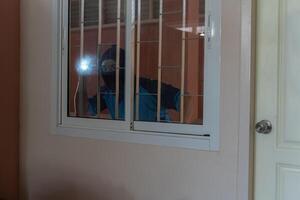 Masked burglar with torch and crowbar breaking and entering into a house, shot with dramatic motion photo