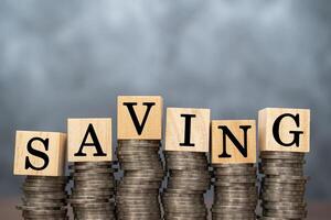 Close up of stacking gold coins and wooden blocks written SAVING on dark background and natural lighting. photo