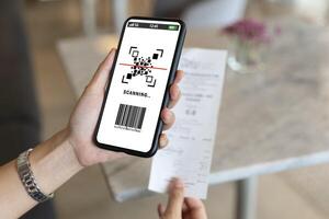 happy Asian woman paying electricity bill hand holding smart phone scanning code on paper, scan the qr code. Scan to get discounts. Using a phone to transfer money photo