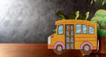 Yellow school bus made of cardboard and plants arranged on students' desks. Blackboard background, back to school concept. There is empty space photo