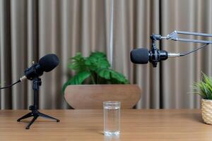 Two microphones for conversing, preparing to talk in a studio. A glass of water placed on a wooden table for hosts. photo