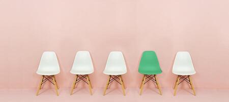 Row of white chairs with contrasting green chairs on a pink background. Five empty chairs on a pink wall photo