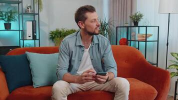 Portrait of young man sitting on sofa, using smartphone share messages on social media application video