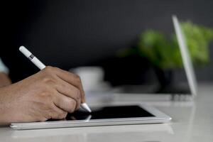 Closeup hand signing or using digital pen on computer tablet on the desk photo