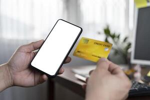 Hand holding credit card and using smartphone. Businessman or entrepreneur working from home. Online shopping, e-commerce, internet banking, spending money. photo