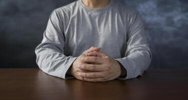 Interlocked fingers, white male hands interlocked on black rustic wood table close up. front view. a man is waiting for negotiations. photo
