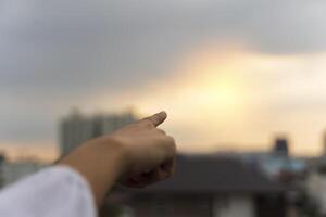 Close-up female hand with index finger up on a background of golden sky with clouds, copy space. photo