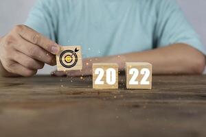 Hand putting wooden cubes 2022 with goal icon on table and white background, copy space. Start new year 2022 with goal plan, goal concept photo