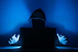 computer hacker with hoodie and obscured face. Hacker in front of his computer. Dark face photo