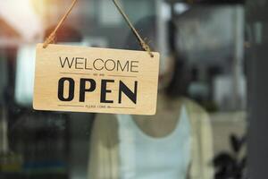 Store owner turning open sign broad through the door glass and ready to service. Open sign hanging front of cafe with colorful bokeh light abstract background. photo