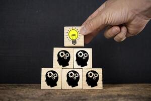 Man holding a cube with a lightbulb symbol placed on a cog-headed businessman. photo