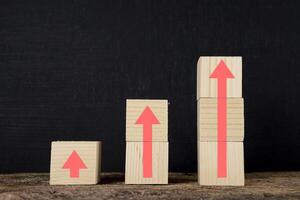 Wooden blocks stacked in steps with red arrows on the table, black background. photo