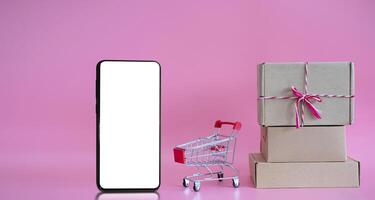 blank screen smartphone. Paper boxes in a trolley with on pink background photo
