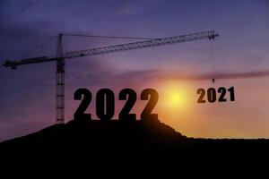 Silhouette of engineer and construction to create lifting crane 2022 on blue sky background. photo