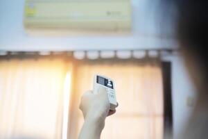 An air conditioner in a room with a young person using a remote control is turning on photo