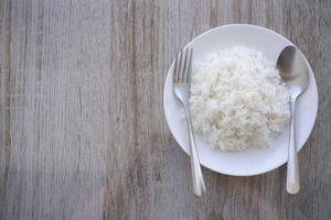 Thai fragrant jasmine rice scooped into served in a white plate on a brown wooden table. photo